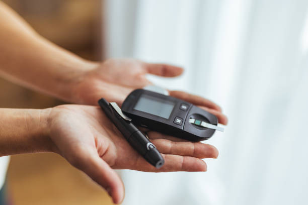 A person holds a glucose meter and lancet pen, essential tools for measuring blood sugar levels in diabetes management. The image conveys health awareness and self-care routines in managing diabetes.