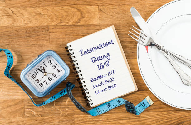 Clock, tape measure, dish with cutlery and notebook with a 16/8 intermittent fasting meal schedule. Concept of intermittent fasting, diet with benefits such as the regeneration mechanism of autophagy.