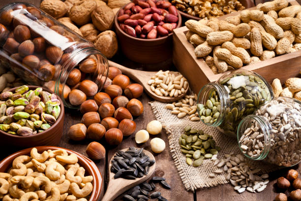 Nuts-001 Horizontal shot of a rustic wood table filled with a large assortment of nuts like pistachios, hazelnut, pine nut, almonds, pumpkin seeds, sunflower seeds, peanuts, cashew and walnuts. Some nuts are in brown bowls and others in glass jars. Predominant color is brown. DSRL studio photo taken with Canon EOS 5D Mk II and Canon EF 100mm f/2.8L Macro IS USM