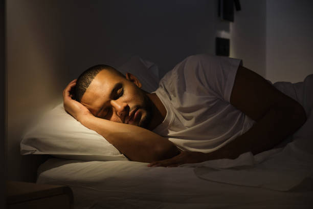 Young man is enjoying a peaceful sleep in his bed, bathed in the warm glow of a bedside lamp