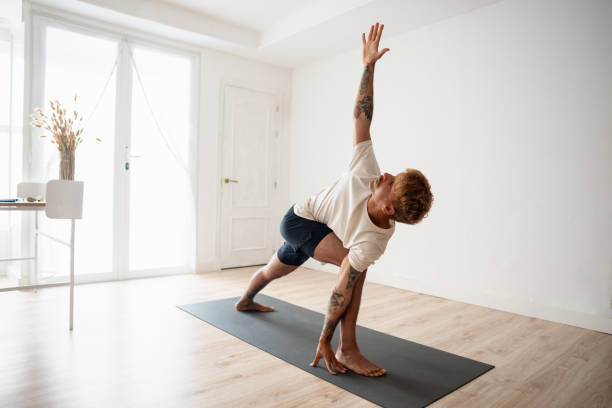 Horizontal photo of a modern man raising arm practicing Triangle pose yoga at home.