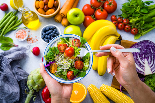Woman eating fresh rainbow colored salad. Multicolored fruits and vegetables background. Healthy eating and dieting concept. High resolution 42Mp studio digital capture taken with SONY A7rII and Zeiss Batis 40mm F2.0 CF lens