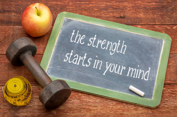 the strength starts in your mind - white chalk text on a slate blackboard against weathered red painted barn wood with a dumbbell, apple and tape measure