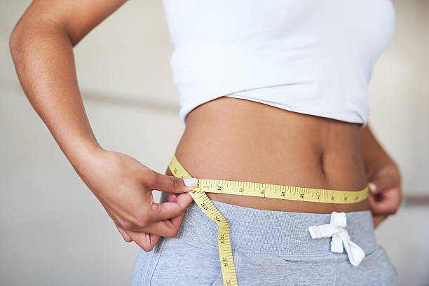 Cropped shot of a young woman measuring her waist in the bathroom