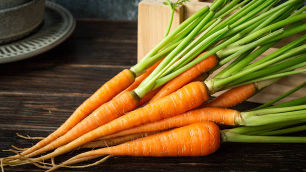 Bright orange carrots with green leaf stalks on an old wooden background in the kitchen.